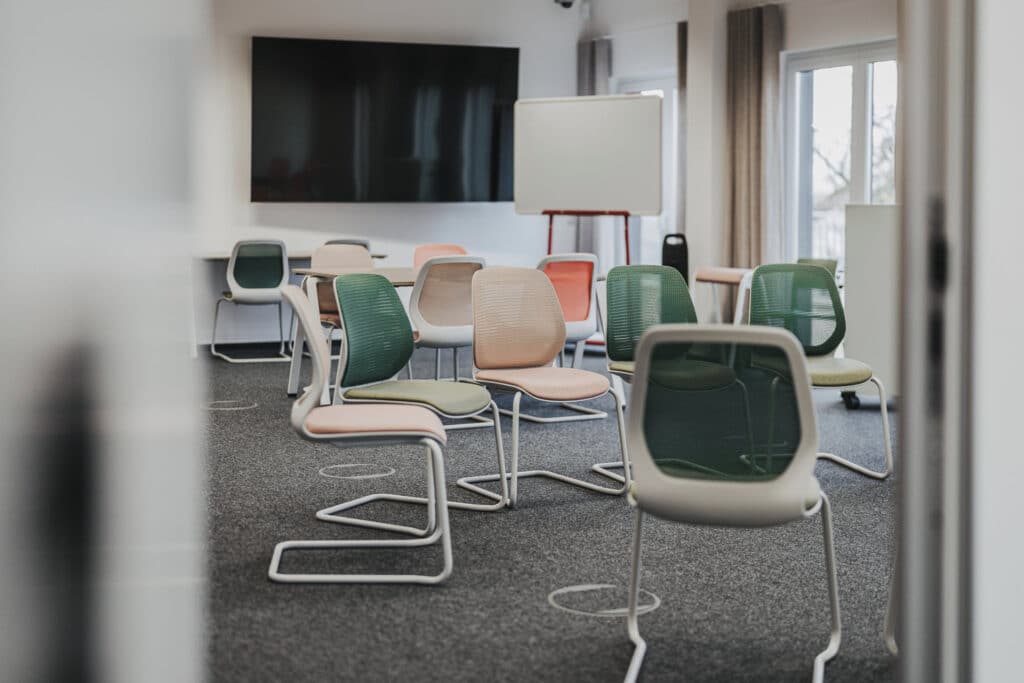 Moderner Konferenzraum mit bunten Stühlen und Flipchart.