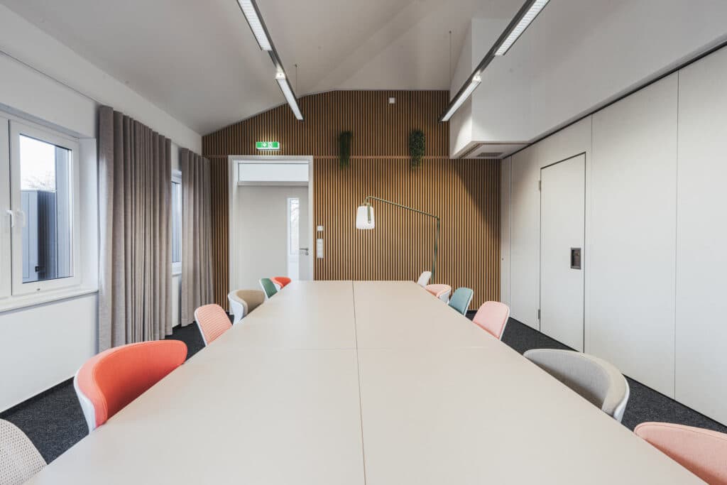 Moderner Konferenzraum mit bunten Stühlen und Holzverkleidung.