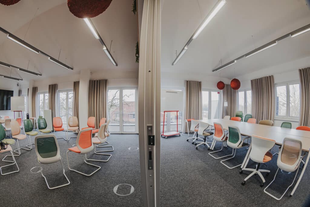 Moderner Konferenzraum mit bunten Stühlen und Tischen.