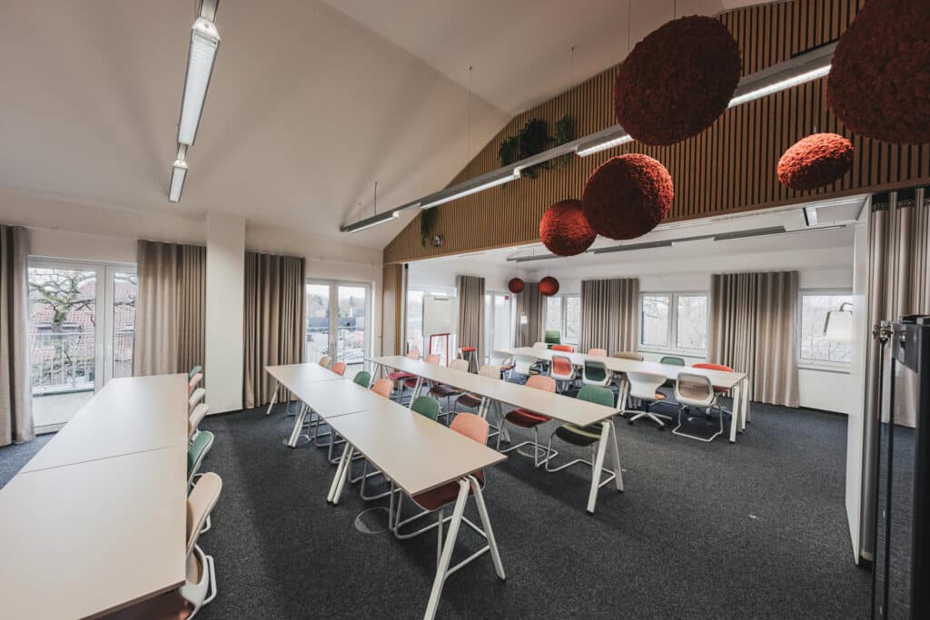 Moderner Konferenzraum mit Tischen und bunten Stühlen.
